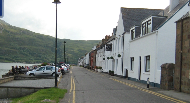 a row of white houses overlooking the flat calm waters of loch broom at ullapool